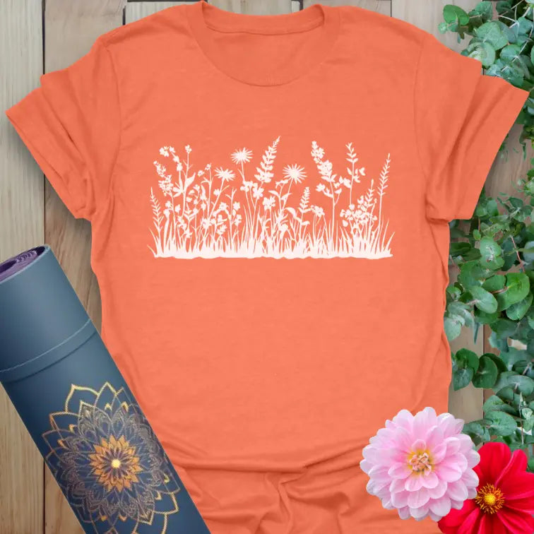 Vibrant orange yoga t-shirt showcasing blooming field flower silhouette for outdoor mindfulness and soulful expression.