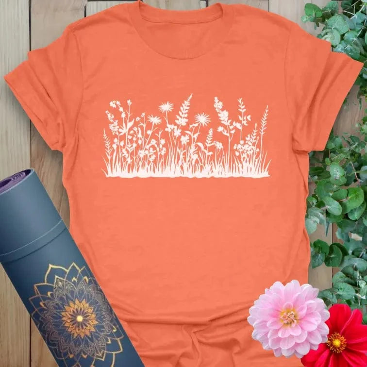 Vibrant orange yoga t-shirt showcasing blooming field flower silhouette for outdoor mindfulness and soulful expression.