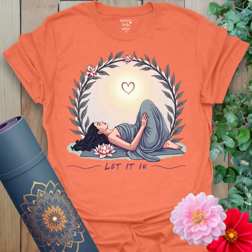 Vibrant orange yoga t-shirt showcasing serene yoga pose, sunrise, and mindful "Let It In" message for conscious, heart-centered living.