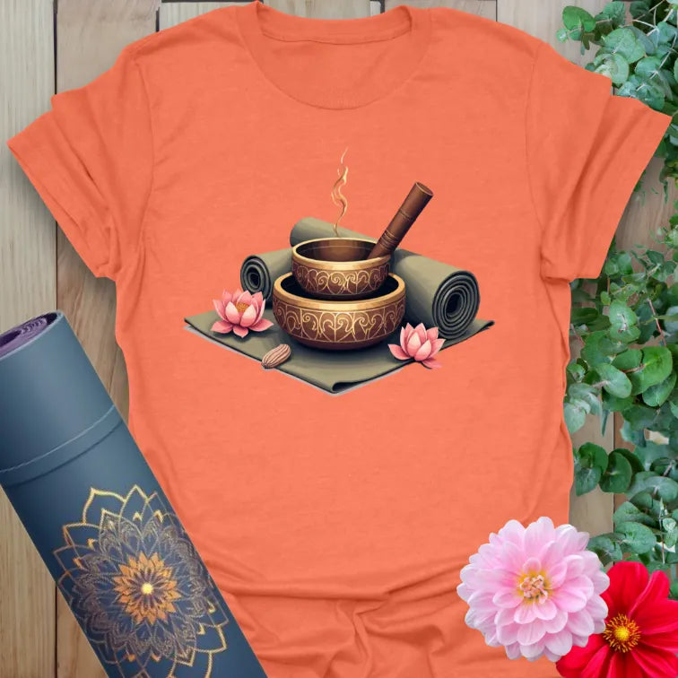 Vibrant orange yoga t-shirt showcasing meditation bowls, incense, and lotus artwork inspiring conscious calm and spiritual living.