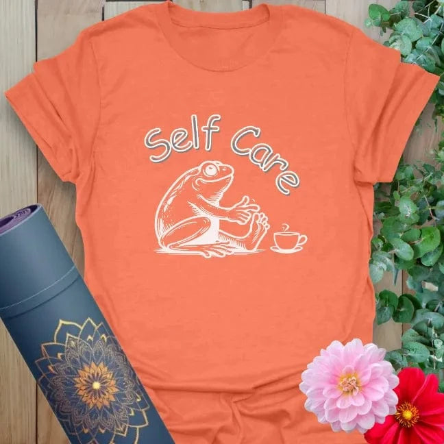 Vibrant orange yoga t-shirt showcasing cozy frog and tea design inspiring joyful self-care and soulful rest.