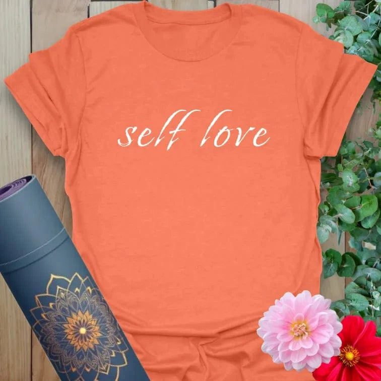 Vibrant orange yoga t-shirt showcasing simple “self love” quote design for joyful, conscious self-care and heartful expression.