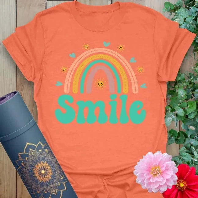 Vibrant orange yoga t-shirt showcasing cheerful rainbow and playful "Smile" design promoting positivity and mindful happiness.