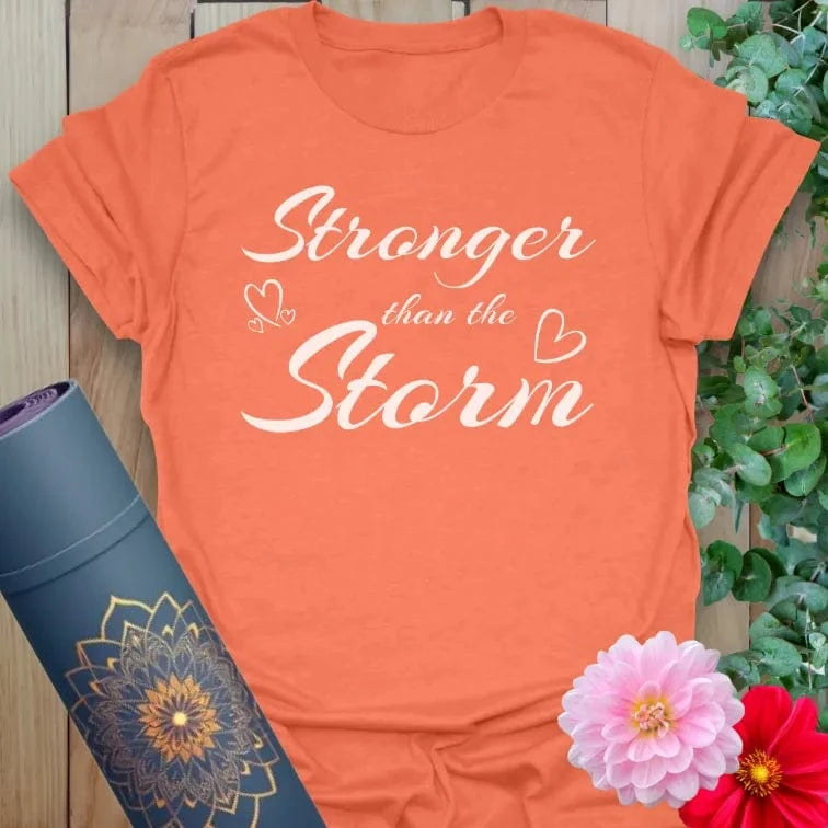 Vibrant orange tee with uplifting “Stronger than the Storm” phrase and gentle graphics for empowered mindfulness.