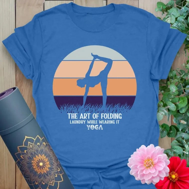 Soft cotton unisex yoga t-shirt featuring playful yogi silhouette and "Art of Folding Laundry" funny yoga quote against a retro sunset backdrop
