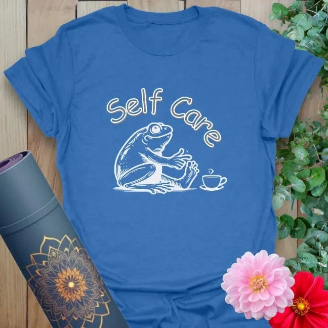 Soft cotton unisex yoga t-shirt featuring whimsical frog in robe with "Self Care" text and teacup illustration for mindful, playful relaxation.