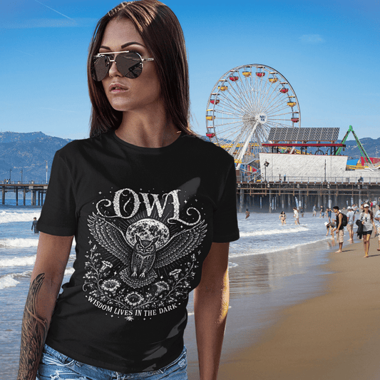 Lifestyle image of woman wearing the Owl T-Shirt at the beach with vintage owl illustration, celestial moon graphic, and mystical aesthetic.