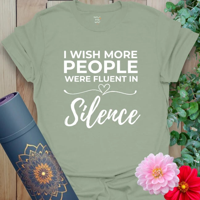 Calm sage green yoga t-shirt featuring "Fluent in Silence" quote and heart design promoting conscious stillness and mindful self-expression.