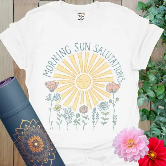 White Morning Sun Salutations T-Shirt with pastel yellow sun, soft floral line art, and arch text. Radiant yoga tee for mindful mornings.