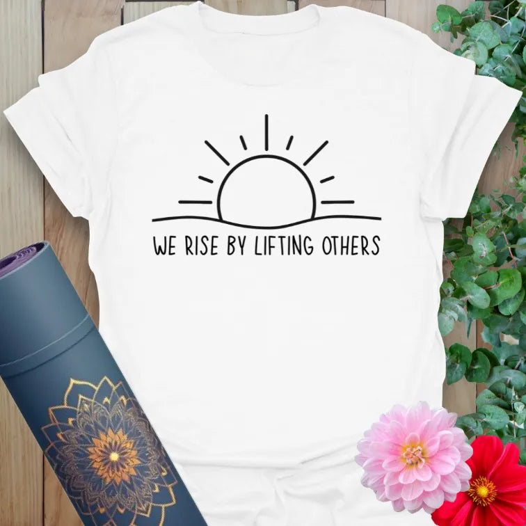 Clean white unisex yoga t-shirt featuring minimalist sunrise artwork and heart-centered "We Rise By Lifting Others" quote.