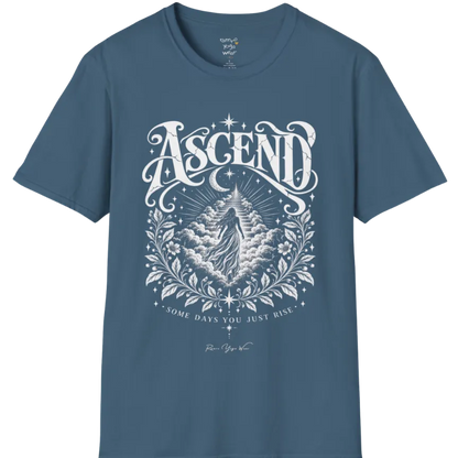 A short sleeved Tee with a figure rising through layered clouds toward a staircase of light, framed by a diamond-shaped botanical border with stars and a crescent moon above. Ascend T-Shirt flat lay is a Gildan 64000 and the color is Indigo Blue.