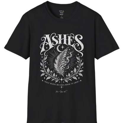 A single feather transforming into ash and ember against a dark starlit background, botanical framing below. Ashes T-Shirt flat lay is a Gildan 64000 and the color is Black.