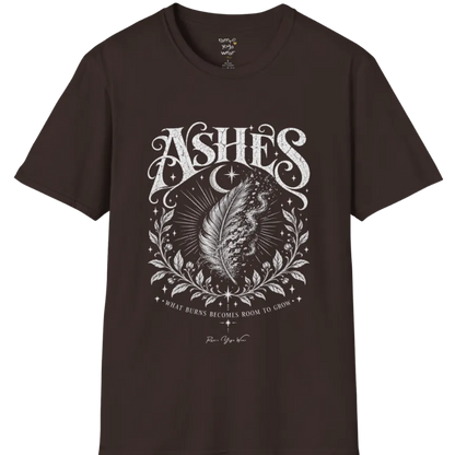 A single feather transforming into ash and ember against a dark starlit background, botanical framing below. Ashes T-Shirt flat lay is a Gildan 64000 and the color is Dark Chocolate.