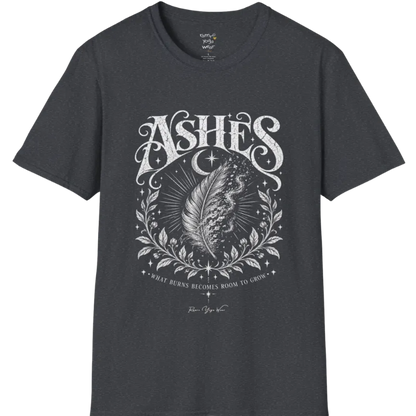 A single feather transforming into ash and ember against a dark starlit background, botanical framing below. Ashes T-Shirt flat lay is a Gildan 64000 and the color is Dark Heather Grey.