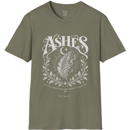 A single feather transforming into ash and ember against a dark starlit background, botanical framing below. Ashes T-Shirt flat lay is a Gildan 64000 and the color is Heather Military Green.