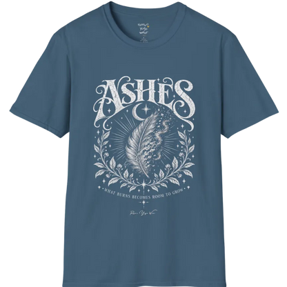 A single feather transforming into ash and ember against a dark starlit background, botanical framing below. Ashes T-Shirt flat lay is a Gildan 64000 and the color is Indigo Blue.