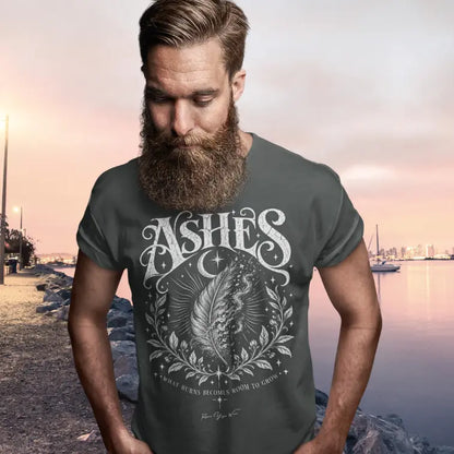 A bearded man stands along a rocky waterfront at sunset with a marina in the background, wearing the Ashes T-Shirt. Ashes T-Shirt is a Gildan 64000 and the color is Dark Heather Grey.