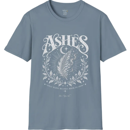 A single feather transforming into ash and ember against a dark starlit background, botanical framing below. Ashes T-Shirt flat lay is a Gildan 64000 and the color is Stone Blue.