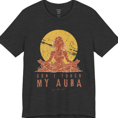 A short sleeved teed called the Aura T-Shirt, flat lay and a Bella + Canvas 3001 shirt. Simply says, Don't Touch My Aura. Design highlights a person meditating with a large bright sun in the background, all in a rustic, distressed illustration. Color is Dark Grey Heather.