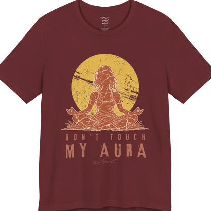A short sleeved teed called the Aura T-Shirt, flat lay and a Bella + Canvas 3001 shirt. Simply says, Don't Touch My Aura. Design highlights a person meditating with a large bright sun in the background, all in a rustic, distressed illustration. Color is Heather Cardinal.