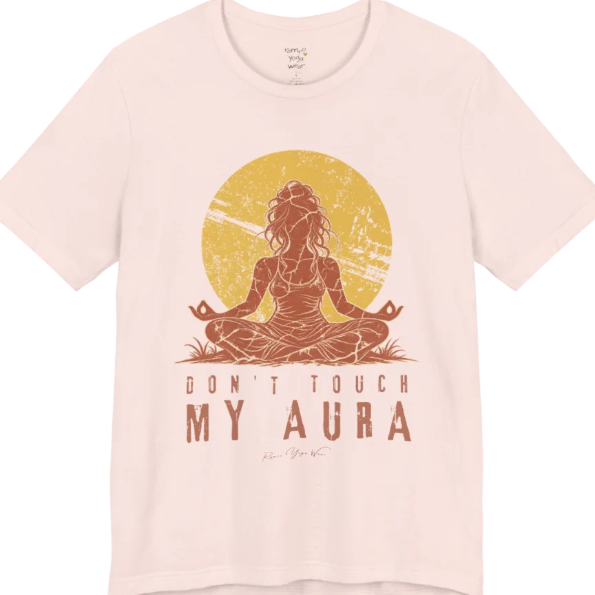 A short sleeved teed called the Aura T-Shirt, flat lay and a Bella + Canvas 3001 shirt. Simply says, Don't Touch My Aura. Design highlights a person meditating with a large bright sun in the background, all in a rustic, distressed illustration. Color is Soft Pink.