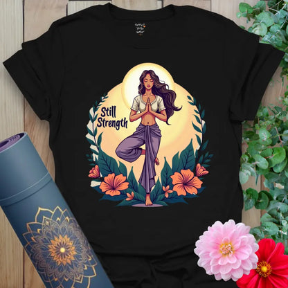 Classic black cotton tee showcasing vibrant yogi in Tree Pose surrounded by florals and “Still Strength” message, perfect for empowered lifestyle wear.