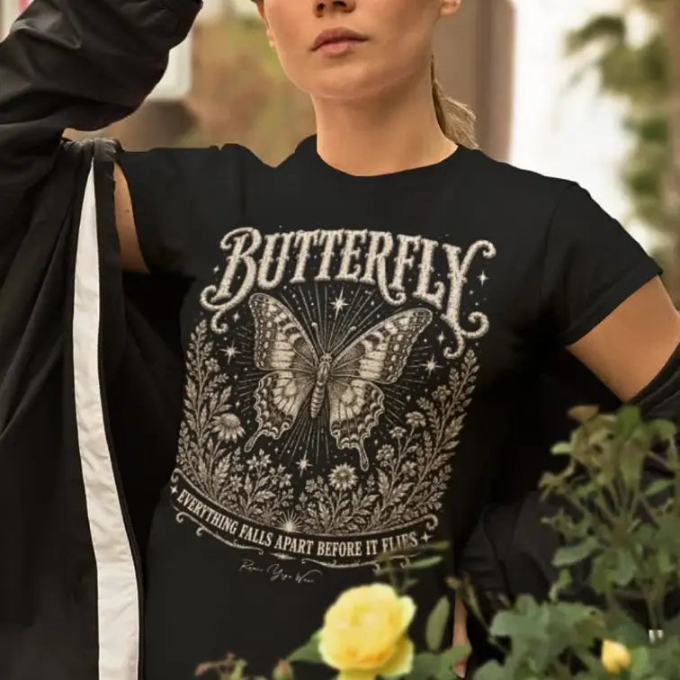 Woman wearing Butterfly T-Shirt outdoors near yellow flowers, adjusting a black wrap over her shoulder