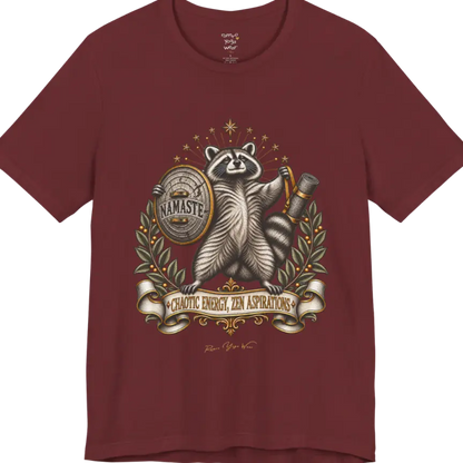 Illustrated raccoon crest holding a shield stamped "Namaste" and a rolled yoga mat, framed by stars and botanical laurel branches. Chaotic Zen T-Shirt flat lay is a Bella+Canvas 3001 and the color in Heather Cardinal.
