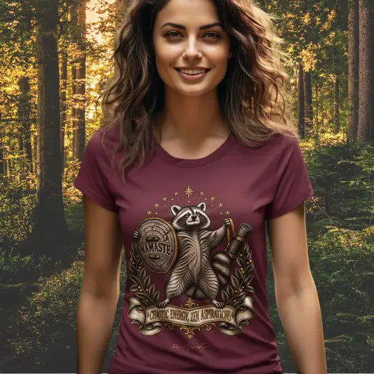 A smiling woman stands in a forest lit by golden-hour sunlight, wearing the Chaotic Zen T-Shirt. Chaotic Zen T-Shirt is a Bella+Canvas 3001 and the color is in the Heather Cardinal color.