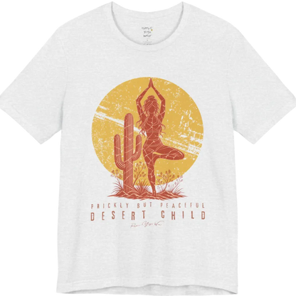 A short sleeved tee called the Desert Child T-Shirt, flat lay and a Bella + Canvas 3001 shirt. Simply says, Prickly But Peaceful, Desert Child. Design highlights a person in Tree Pose beside a desert cactus, with a large distressed sun in the background, in a rustic, distressed illustration. Color is Ash.