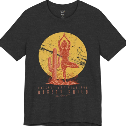 A short sleeved tee called the Desert Child T-Shirt, flat lay and a Bella + Canvas 3001 shirt. Simply says, Prickly But Peaceful, Desert Child. Design highlights a person in Tree Pose beside a desert cactus, with a large distressed sun in the background, in a rustic, distressed illustration. Color is Dark Grey Heather.