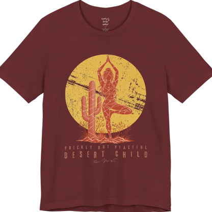 A short sleeved tee called the Desert Child T-Shirt, flat lay and a Bella + Canvas 3001 shirt. Simply says, Prickly But Peaceful, Desert Child. Design highlights a person in Tree Pose beside a desert cactus, with a large distressed sun in the background, in a rustic, distressed illustration. Color is Heather Cardinal.