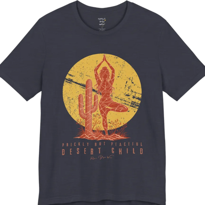 A short sleeved tee called the Desert Child T-Shirt, flat lay and a Bella + Canvas 3001 shirt. Simply says, Prickly But Peaceful, Desert Child. Design highlights a person in Tree Pose beside a desert cactus, with a large distressed sun in the background, in a rustic, distressed illustration. Color is Heather Midnight Navy.