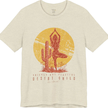 A short sleeved tee called the Desert Child T-Shirt, flat lay and a Bella + Canvas 3001 shirt. Simply says, Prickly But Peaceful, Desert Child. Design highlights a person in Tree Pose beside a desert cactus, with a large distressed sun in the background, in a rustic, distressed illustration. Color is Heather Prism Natural.