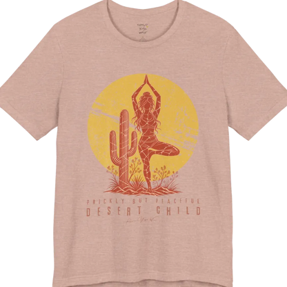 A short sleeved tee called the Desert Child T-Shirt, flat lay and a Bella + Canvas 3001 shirt. Simply says, Prickly But Peaceful, Desert Child. Design highlights a person in Tree Pose beside a desert cactus, with a large distressed sun in the background, in a rustic, distressed illustration. Color is Heather Prism Peach.