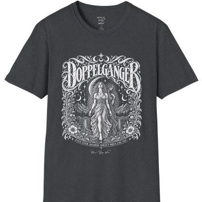 A short sleeved tee called the Doppelganger T-Shirt, flat lay and a Gildan 64000 shirt. Simply says, Even Your Shadow Doesn't Move Like You. Design highlights a woman standing before a crescent moon with a second shadow-self figure behind her, framed by mountains, florals, and ornate engraved linework border. Color is Dark Heather Grey.