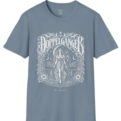A short sleeved tee called the Doppelganger T-Shirt, flat lay and a Gildan 64000 shirt. Simply says, Even Your Shadow Doesn't Move Like You. Design highlights a woman standing before a crescent moon with a second shadow-self figure behind her, framed by mountains, florals, and ornate engraved linework border. Color is Stone Blue.
