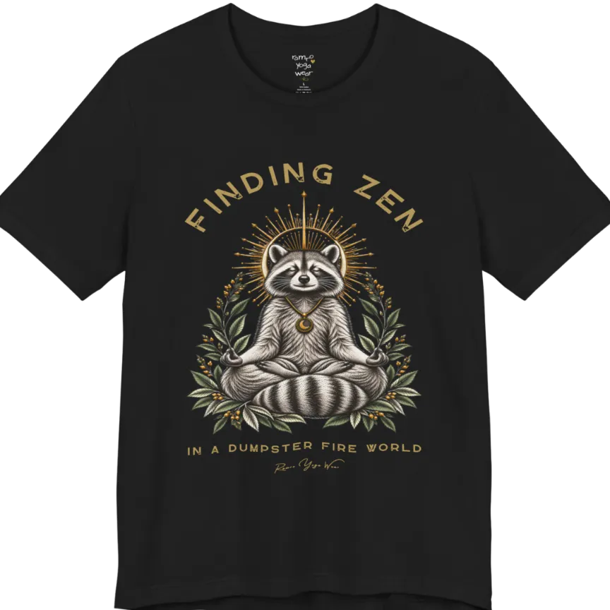 A short sleeved Tee of a meditating raccoon illustration with a gold sunburst halo and botanical leaf framing. Dumpster T-Shirt flat lay is a Bella+Canvas 3001 and the color is Black.