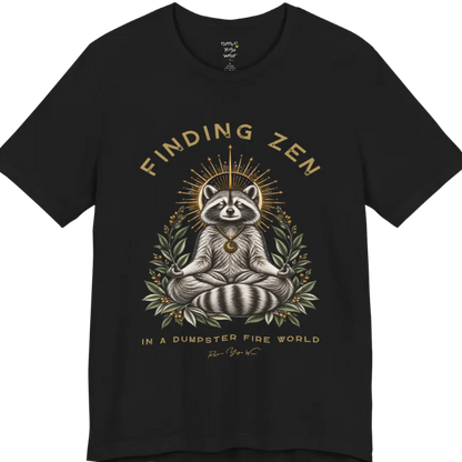 A short sleeved Tee of a meditating raccoon illustration with a gold sunburst halo and botanical leaf framing. Dumpster T-Shirt flat lay is a Bella+Canvas 3001 and the color is Black.