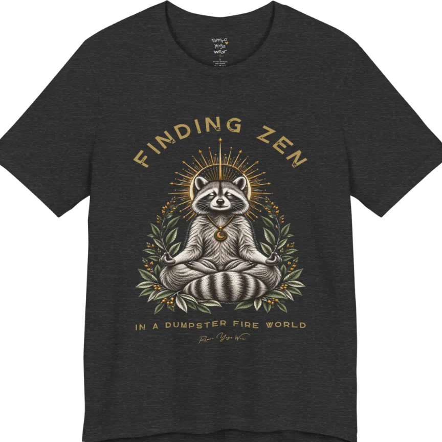 A short sleeved Tee of a meditating raccoon illustration with a gold sunburst halo and botanical leaf framing. Dumpster T-Shirt flat lay is a Bella+Canvas 3001 and the color is Dark Grey Heather.