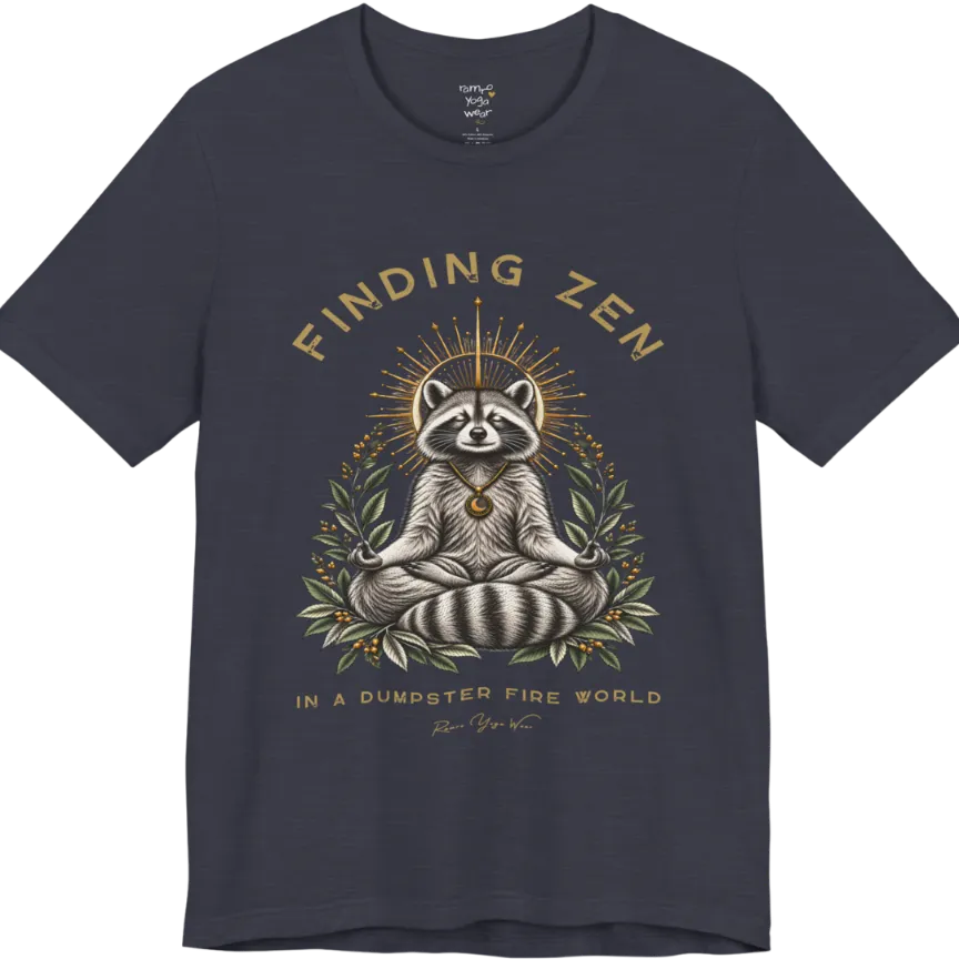 A short sleeved Tee of a meditating raccoon illustration with a gold sunburst halo and botanical leaf framing. Dumpster T-Shirt flat lay is a Bella+Canvas 3001 and the color is Heather Midnight Navy.
