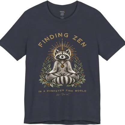 A short sleeved Tee of a meditating raccoon illustration with a gold sunburst halo and botanical leaf framing. Dumpster T-Shirt flat lay is a Bella+Canvas 3001 and the color is Heather Midnight Navy.