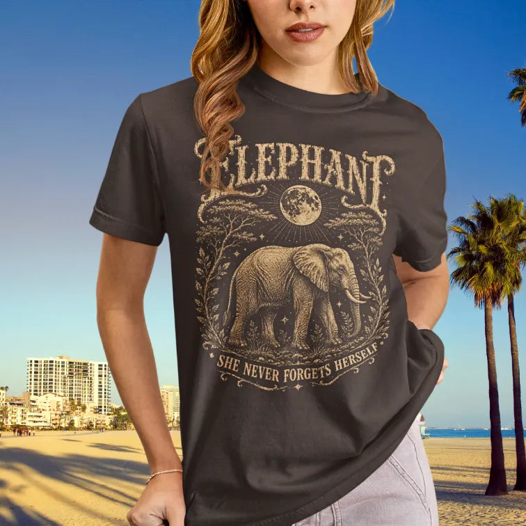 Person wearing the Elephant T-Shirt in Dark Chocolate, standing outdoors near palm trees with the beach in the background — Wild Animals collection by Ramro Yoga Wear.