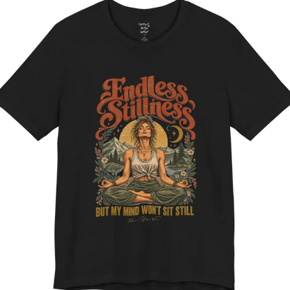 A short sleeved tee, showing an Illustration of a woman seated in lotus meditation pose in front of mountains, pine trees, and a crescent moon, framed by botanical leaves and flowers. Endless T-Shirt flat lay is a Bella+Canvas 3001 and the color is Black.