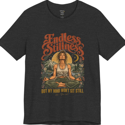 A short sleeved tee, showing an Illustration of a woman seated in lotus meditation pose in front of mountains, pine trees, and a crescent moon, framed by botanical leaves and flowers. Endless T-Shirt flat lay is a Bella+Canvas 3001 and the color is Dark Grey Heather.