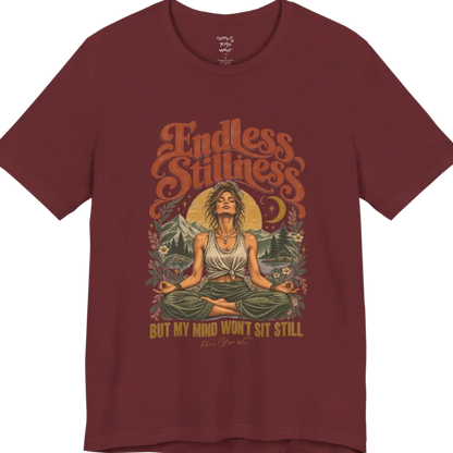 A short sleeved tee, showing an Illustration of a woman seated in lotus meditation pose in front of mountains, pine trees, and a crescent moon, framed by botanical leaves and flowers. Endless T-Shirt flat lay is a Bella+Canvas 3001 and the color is Heather Cardinal.