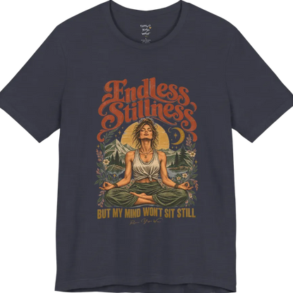 A short sleeved tee, showing an Illustration of a woman seated in lotus meditation pose in front of mountains, pine trees, and a crescent moon, framed by botanical leaves and flowers. Endless T-Shirt flat lay is a Bella+Canvas 3001 and the color is Heather Midnight Navy.