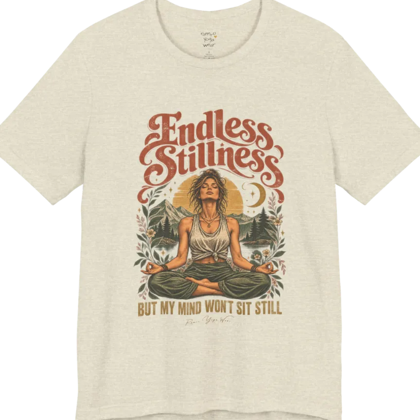 A short sleeved tee, showing an Illustration of a woman seated in lotus meditation pose in front of mountains, pine trees, and a crescent moon, framed by botanical leaves and flowers. Endless T-Shirt flat lay is a Bella+Canvas 3001 and the color is Heather Prism Natural.
