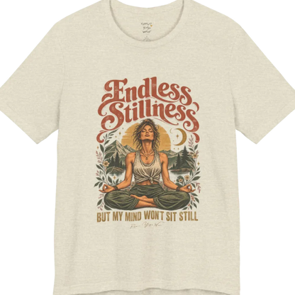 A short sleeved tee, showing an Illustration of a woman seated in lotus meditation pose in front of mountains, pine trees, and a crescent moon, framed by botanical leaves and flowers. Endless T-Shirt flat lay is a Bella+Canvas 3001 and the color is Heather Prism Natural.
