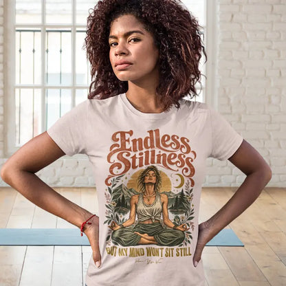 A woman stands with her hands on her hips on a yoga mat in a bright studio, wearing the Endless T-Shirt. Endless T-Shirt is a Bella+Canvas 3001 and the color is Soft Pink